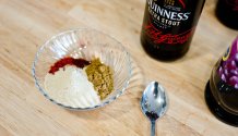 Rezept Foto von der rauchigen Barbecue Sauce. Das Foto zeigt ein Schneidebrett und darauf eine Variaten aus den Gewürzen für die BBQ Soße. Im Hintergrund steht eine Flasche Schwarzbier die als Grundlage für die Sauce benötigt wird.