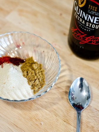 Rezept Foto von der rauchigen Barbecue Sauce. Das Foto zeigt ein Schneidebrett und darauf eine Variaten aus den Gewürzen für die BBQ Soße. Im Hintergrund steht eine Flasche Schwarzbier die als Grundlage für die Sauce benötigt wird.