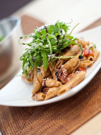 Rezept Foto vom italienischen Nudelsalat. Das Foto zeigt eine Nahaufnahme von einem gewölbtem Teller mit reichlich Nudelsalat darauf. Der Nudelsalat ist mit frischem Ruccola und Balsamico Creme garniert worden.