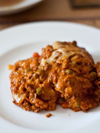Rezept Foto der italienischen Lasagne. Das Foto zeigt die dampfende frisch aus der Form gestochene Lasagne. Angerichtet auf einem eierschalen farbenen runden Teller.