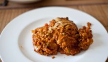 Rezept Foto der italienischen Lasagne. Das Foto zeigt die dampfende frisch aus der Form gestochene Lasagne. Angerichtet auf einem eierschalen farbenen runden Teller.