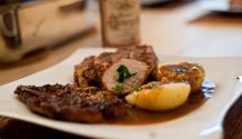 Ansicht des angerichteteten Rezepts: Schweinebraten mit Kümmelbiersöße auf einem gewölbten Teller. Im Hintergrund ist eine Flasche Bier zu sehen, das auch für die Sauce verwendet wurde.