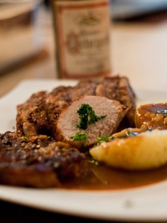 Ansicht des angerichteteten Rezepts: Schweinebraten mit Kümmelbiersöße auf einem gewölbten Teller. Im Hintergrund ist eine Flasche Bier zu sehen, das auch für die Sauce verwendet wurde.
