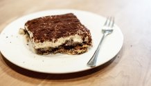 Eine Detailaufnahme der angerichteten Tiramisu auf einem kleinen runden Teller mit einer Kuchengabel. Man sieht die feine Schicht Kakao Pulver und die fluffige Eierlikör Creme.