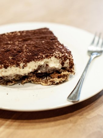 Eine Detailaufnahme der angerichteten Tiramisu auf einem kleinen runden Teller mit einer Kuchengabel. Man sieht die feine Schicht Kakao Pulver und die fluffige Eierlikör Creme.