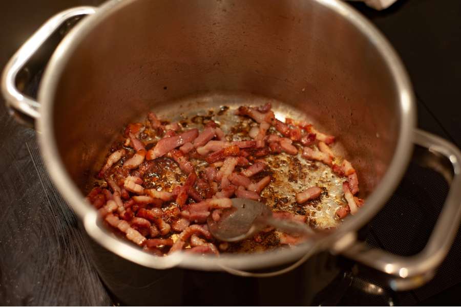 Rezept Foto Lauchzwiebelkuchen backen und genießen. Speck wird in einem kleinen Topf auf dem Ofen scharf angebraten.