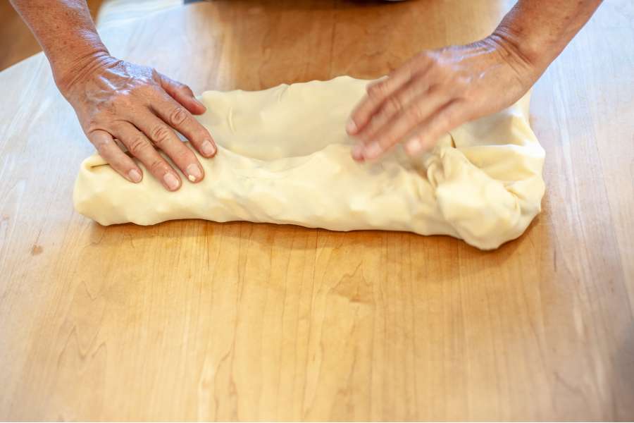 Rezept Foto Oberpfälzer Milchrahm Apfelstrudel. Mama Siglinde faltet den Teig an den Ecken ein und formt es langsam zu einem langen Schlauch.