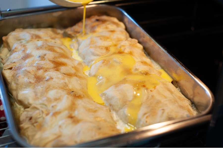 Rezept Foto Oberpfälzer Milchrahm Apfelstrudel. Mama Siglinde schüttet das gequirlte Ei langsam über den zweiten Strudel.