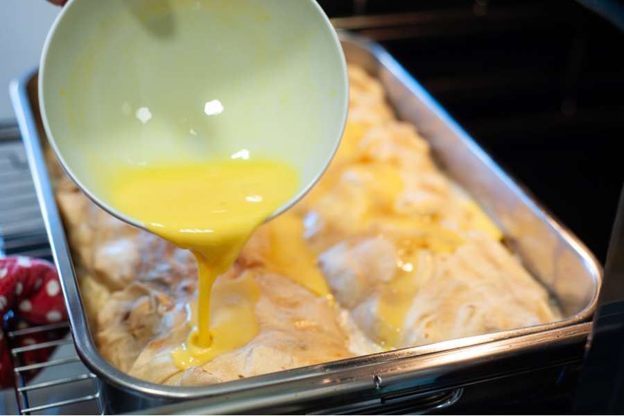 Rezept Foto Oberpfälzer Milchrahm Apfelstrudel. Nahaufnahme Mama Siglinde schüttet das gequirlte Ei langsam über den ersten Strudel.