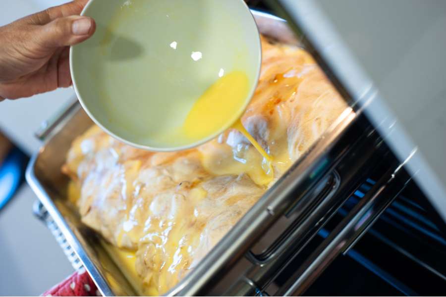 Rezept Foto Oberpfälzer Milchrahm Apfelstrudel. Nahaufnahme Mama Siglinde schüttet das gequirlte Ei langsam über den zweiten Strudel.