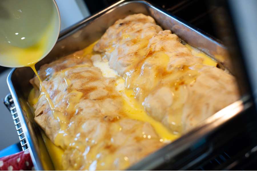 Rezept Foto Oberpfälzer Milchrahm Apfelstrudel. Seitenaufnahme Mama Siglinde schüttet das gequirlte Ei langsam über den ersten Strudel.