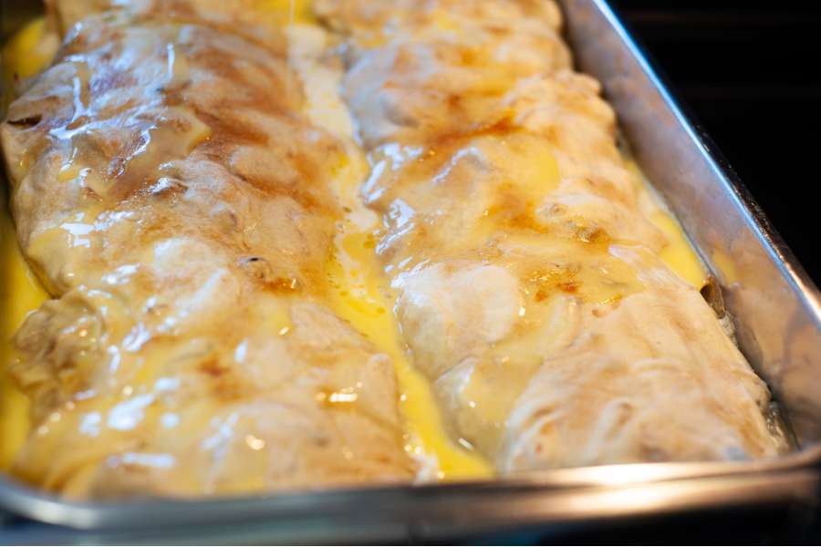Rezept Foto Oberpfälzer Milchrahm Apfelstrudel. Seitenaufnahme Mama Siglinde schüttet das gequirlte Ei langsam über den zweiten Strudel.