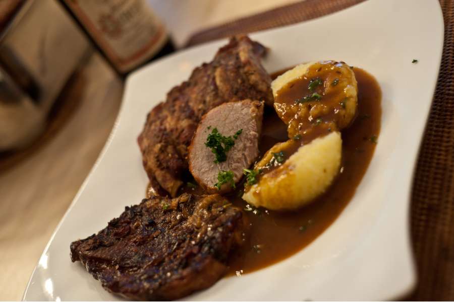Rezept Foto Bayerischer Schweinebraten in der Kümmelbiersoße. Das fertige Gericht angerichtet auf einem geschwungenen Teller. Zwei Stücke Schweinebraten und einen Kartoffelknödel mit Kräutern bestreut.