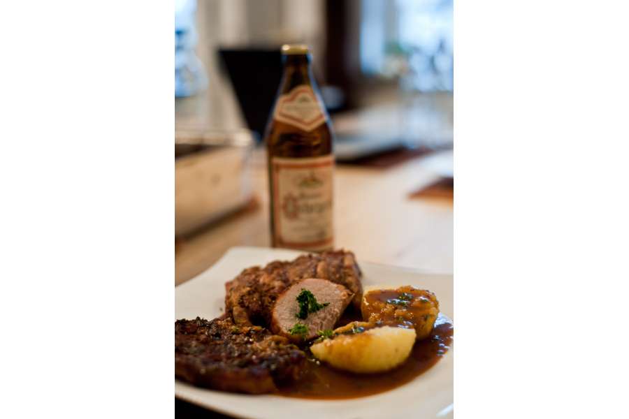Rezept Foto Bayerischer Schweinebraten in der Kümmelbiersoße. Der fertige Schweinebraten angerichtet auf einem geschwungenen Teller. Zwei Stücke Schweinebraten und einen Kartoffelknödel mit Kräutern bestreut. Lecker!