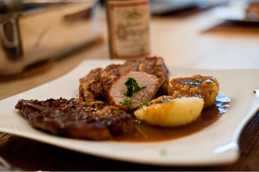 Rezept Foto Bayerischer Schweinebraten in der Kümmelbiersoße. Der fertige Schweinebraten angerichtet auf einem Teller. Zwei Stücke Braten und einen Knödel mit Kräutern bestreut.