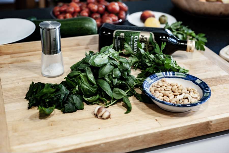 Rezept Foto Kräuter und Garten Pesto. Seitenansicht Schneidebrett mit Olivenöl Flasche einer Parmesan Reibe und den Kräutern darauf.