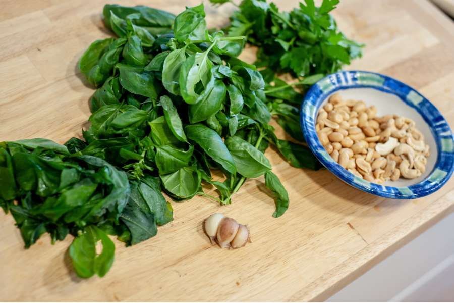 Rezept Foto Kräuter und Garten Pesto. Frisches Garten Basilikum liegt zusammen mit mehreren Knoblauchzehen auf dem Schneidebrett.