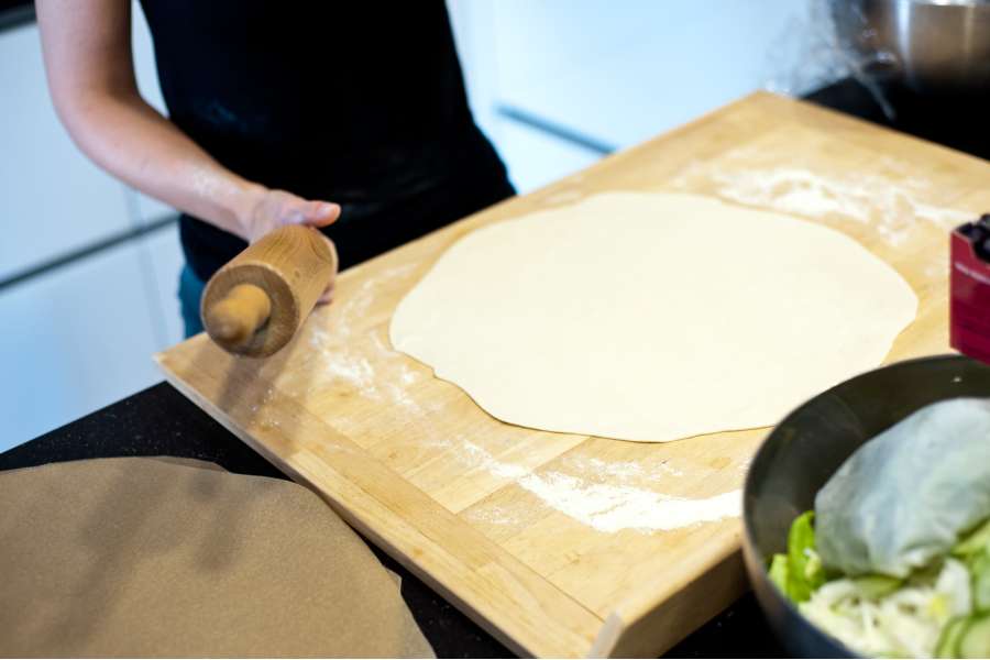 Rezept Foto Grillpizza und Ofenpizza Italien. Katharina rollt den Teig zum Schluss auf dem Schneidebrett aus. Der Teig ist lange und dünn.
