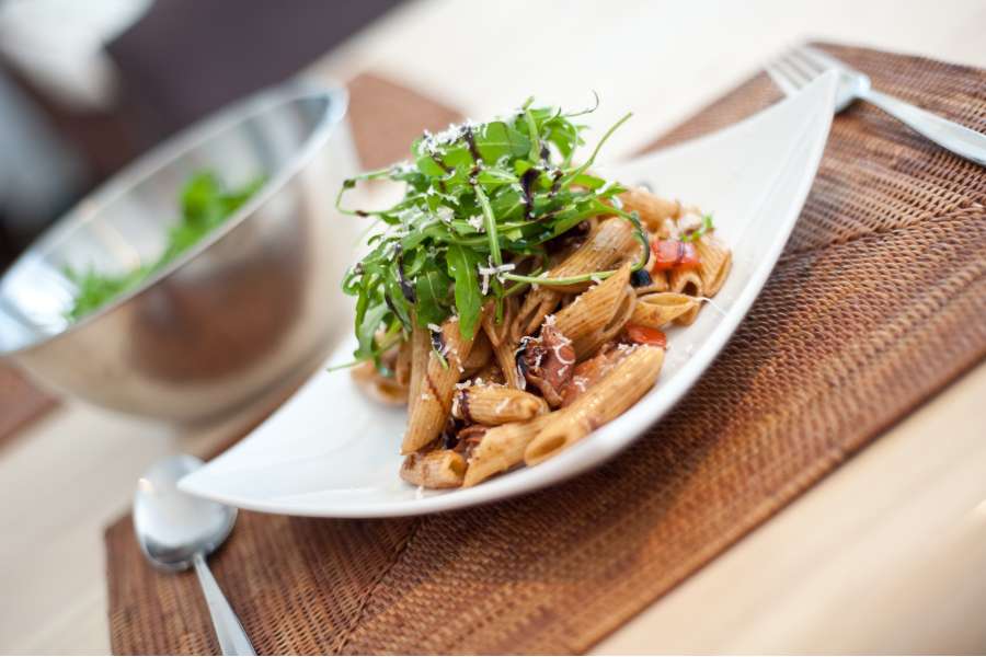 Rezept Foto Italienischer Nudelsalat. Der Antipasti Salat ist auf einem geschwungenem Teller angerichtet und mit Ruccola garniert.