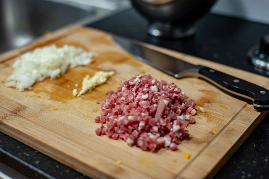 Rezept Foto Kürbis Quiche selber machen. Auf einem Schneidebrett wurden Zwiebelchen und Schinken Speck für den Belag der Quiche gehackt.