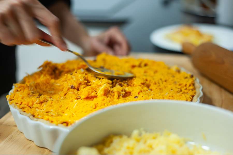 Rezept Foto Kürbis Quiche selber machen. Katharina drückt die Kürbis Speck Masse vorsichtig in die Quicheform.
