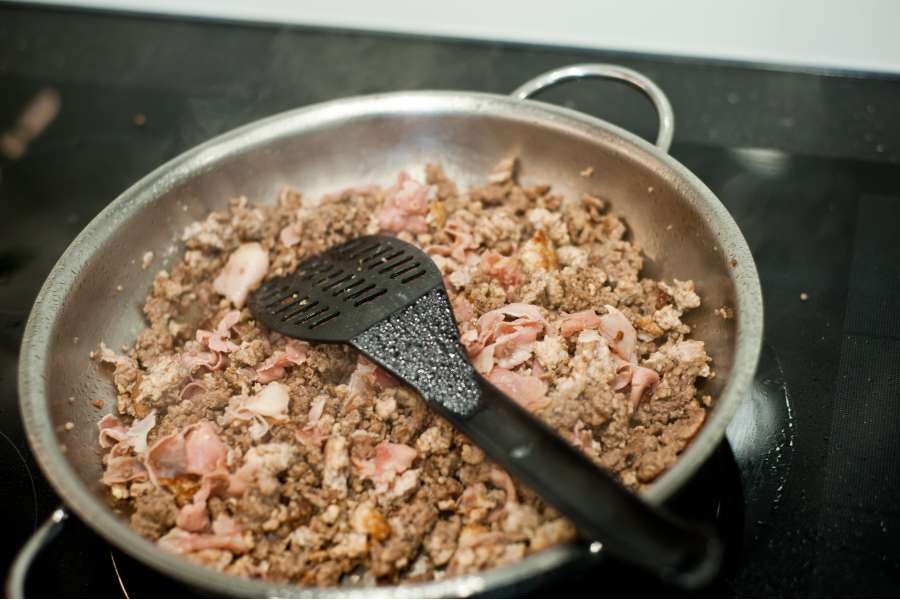 Rezept Foto Lasagne selber machen. In einer großen Edelstahlpfanne werden erst das Hackfleisch und dann der Schinken angebräunt.