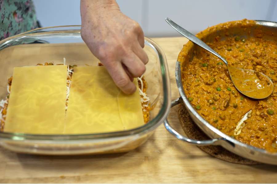 Rezept Foto Lasagne selber machen. Mama Siglinde legt eine neue Schicht Lasagne Nudeln auf die Hackfleisch Schicht der Lasagne auf.