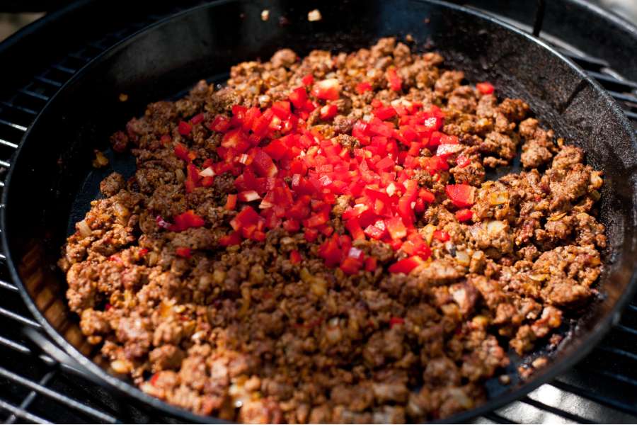 Rezept Foto Mexikansiche Enchillada. Das scharf angegrillte Hackfleisch ist schön braun geworden, nun kommen die zerkleinerten Paprikas dazu.