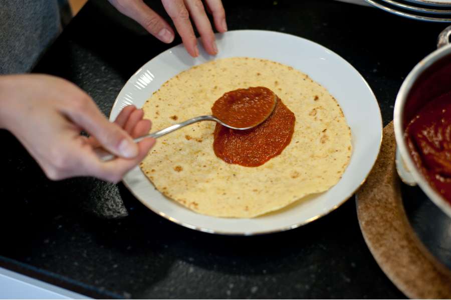 Rezept Foto Mexikansiche Enchillada. Katharina streicht die Tomatensauce hauch dünn auf die Maismehltortillas.