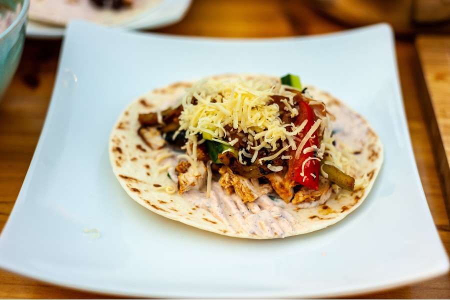 Rezept Foto Mexikansiche Grill Fajitas. Die Fajitas werden gerade auf einem kleinen Teller gelegt und mit den Zutaten befüllt. Gleich wird gegessen.