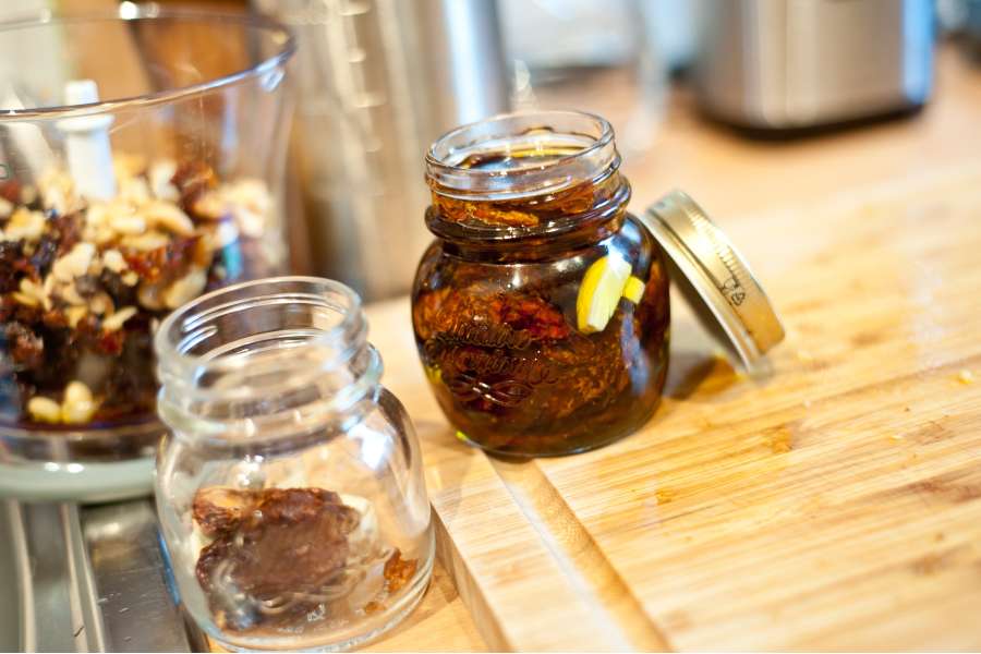 Rezept Foto Rotes Pesto Rosso. Ein paar Einweckgläser stehen auf dem Schneidebrett und werden mit Oliveöl befüllt.