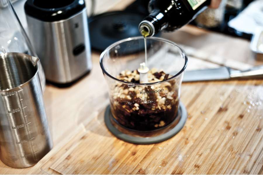 Rezept Foto Rotes Pesto Rosso. Die Zutaten kommen in einen Multihacker und das Olivenöl wird gerade hinzugefügt. Gleich wird das Pesto zerkleinert.