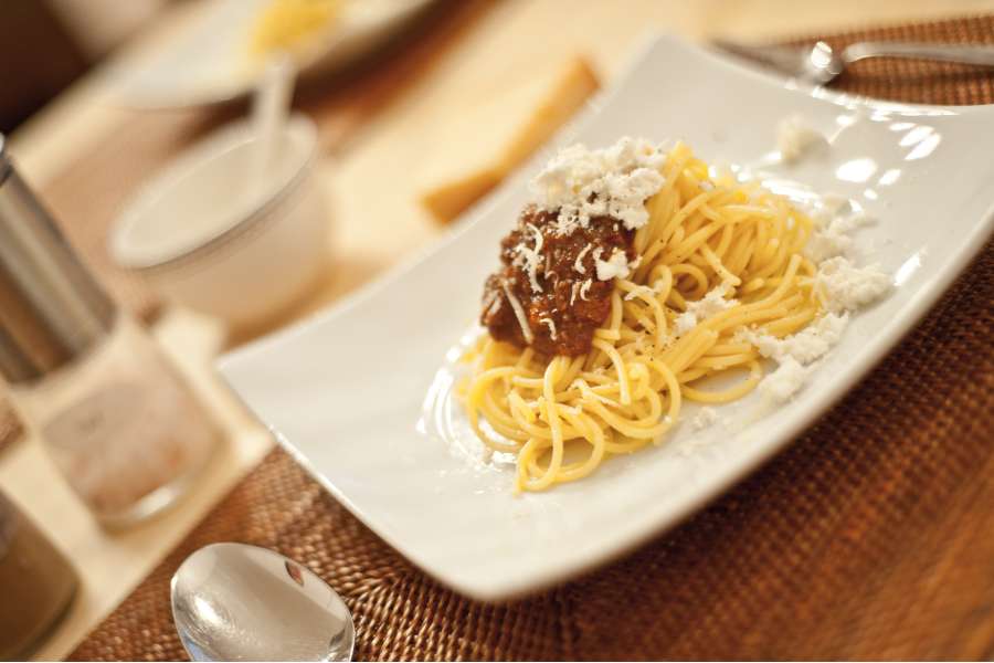 Rezept Foto Rotes Pesto Rosso. Seitenaufnahme des Rezepts, angerichtet auf einem Teller. Ein kleiner Haufen Sphaghetti und ein Klecks Rotes Pesto darauf. Als Krönung frischer Parmesan.