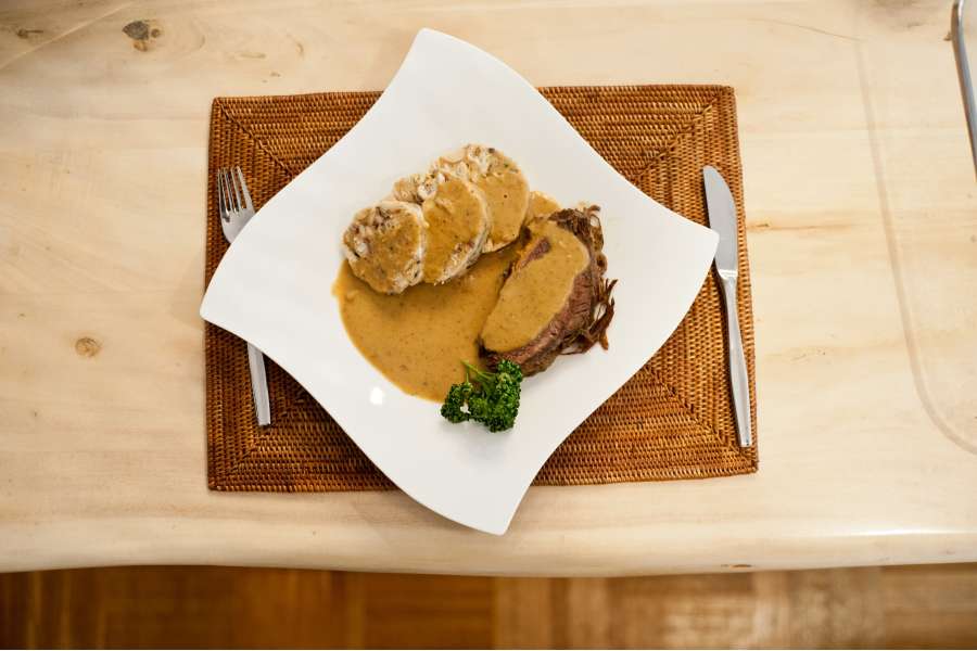 Rezept Foto Sauerbraten mit Serviettenknödel. Draufsicht auf den angerichteten Teller mit zwei Stücken Sauerbraten, Serviettenknödel und ganz viel Soße.