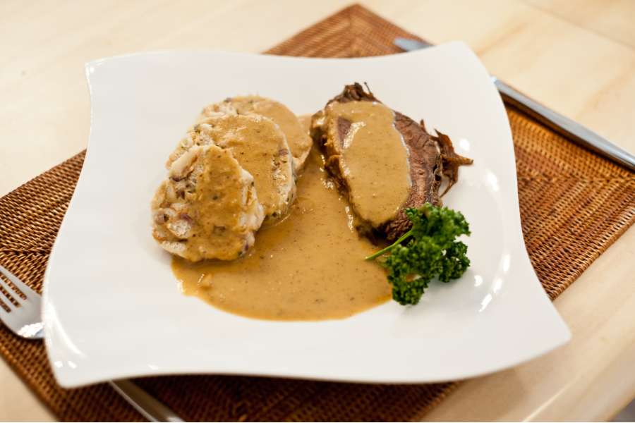 Rezept Foto Sauerbraten mit Serviettenknödel. Das Rezept wird gerade auf einen Teller serviert. Zwei leckere Serviettenknödel und zwei Scheiben Sauerbraten mit ganz viel rahmiger Sauce warten darauf verzehrt zu werden.