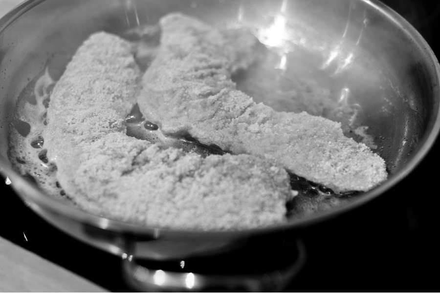 Nahaufnahme in Schwarz/Weiss. Wiener Schnitzel bereits mit Semmelbrösel paniert in einer Edelstahlpfanne mit viel Butter. Das Schnitzel wird gerade auf mittlerer Temperatur herausgebraten.