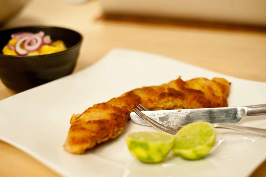 Wiener Schnitzel gold gelb herausgebraten auf einem Teller serviert mit einer Limette angerichtet.