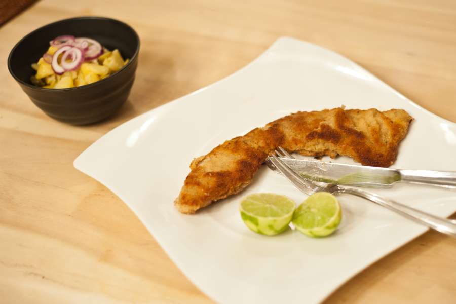 Wiener Schnitzel gold gelb herausgebraten auf einem Teller serviert und mit dem Kartoffelsalat daneben, bereit zum Essen.